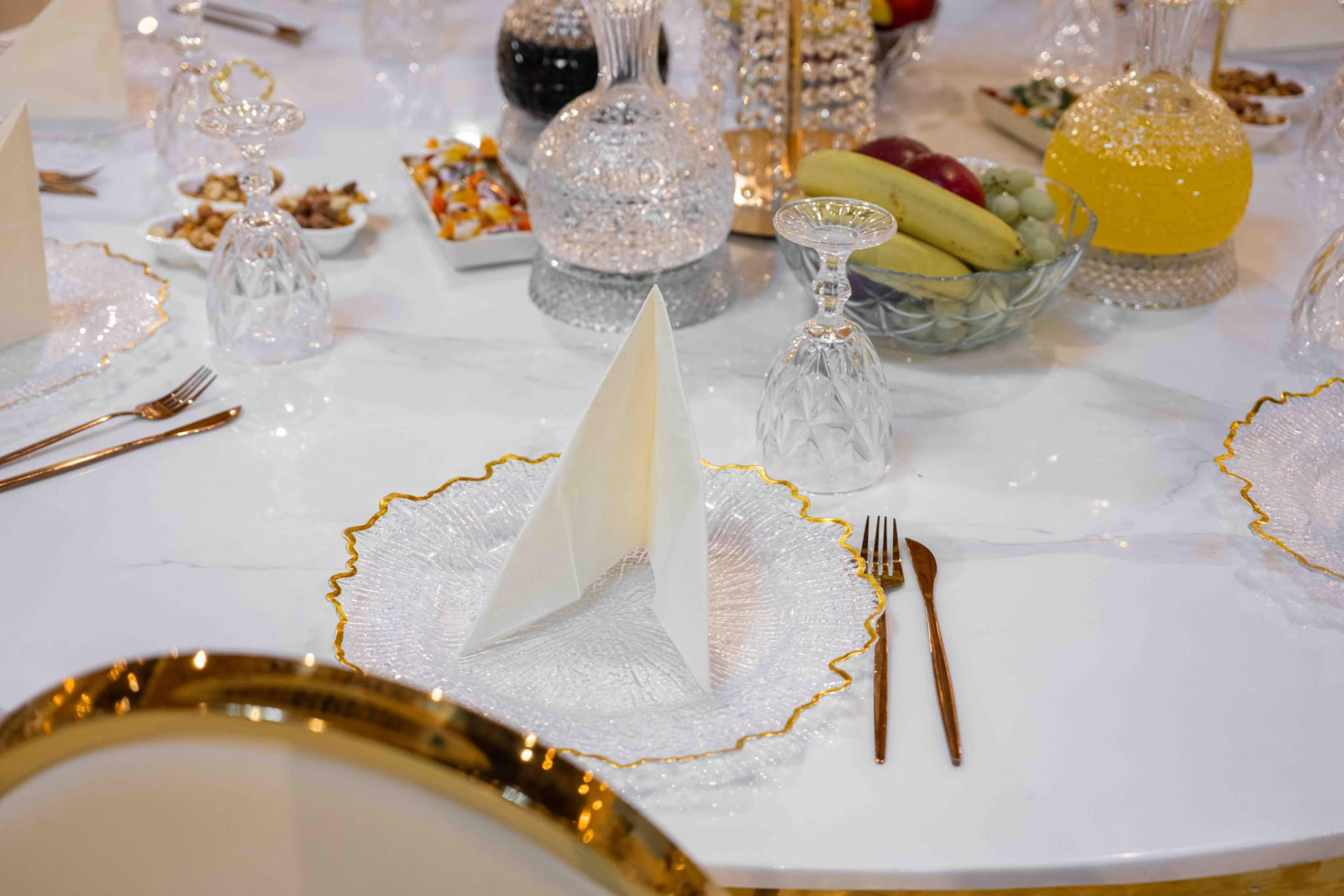 Gedeckter Platz mit goldumrandetem Glasteller, weißer Serviette und goldenem Besteck