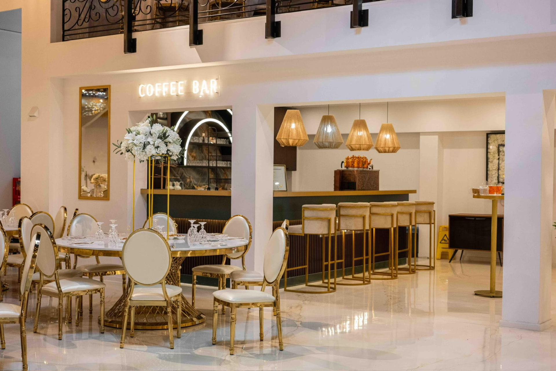 Coffee Bar mit weißen Blumen, goldenen Barhockern und gedeckten Tischen